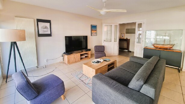 Ein Wohnzimmer mit Sofa, Sessel, Couchtisch, Fernseher und Deckenventilator.
