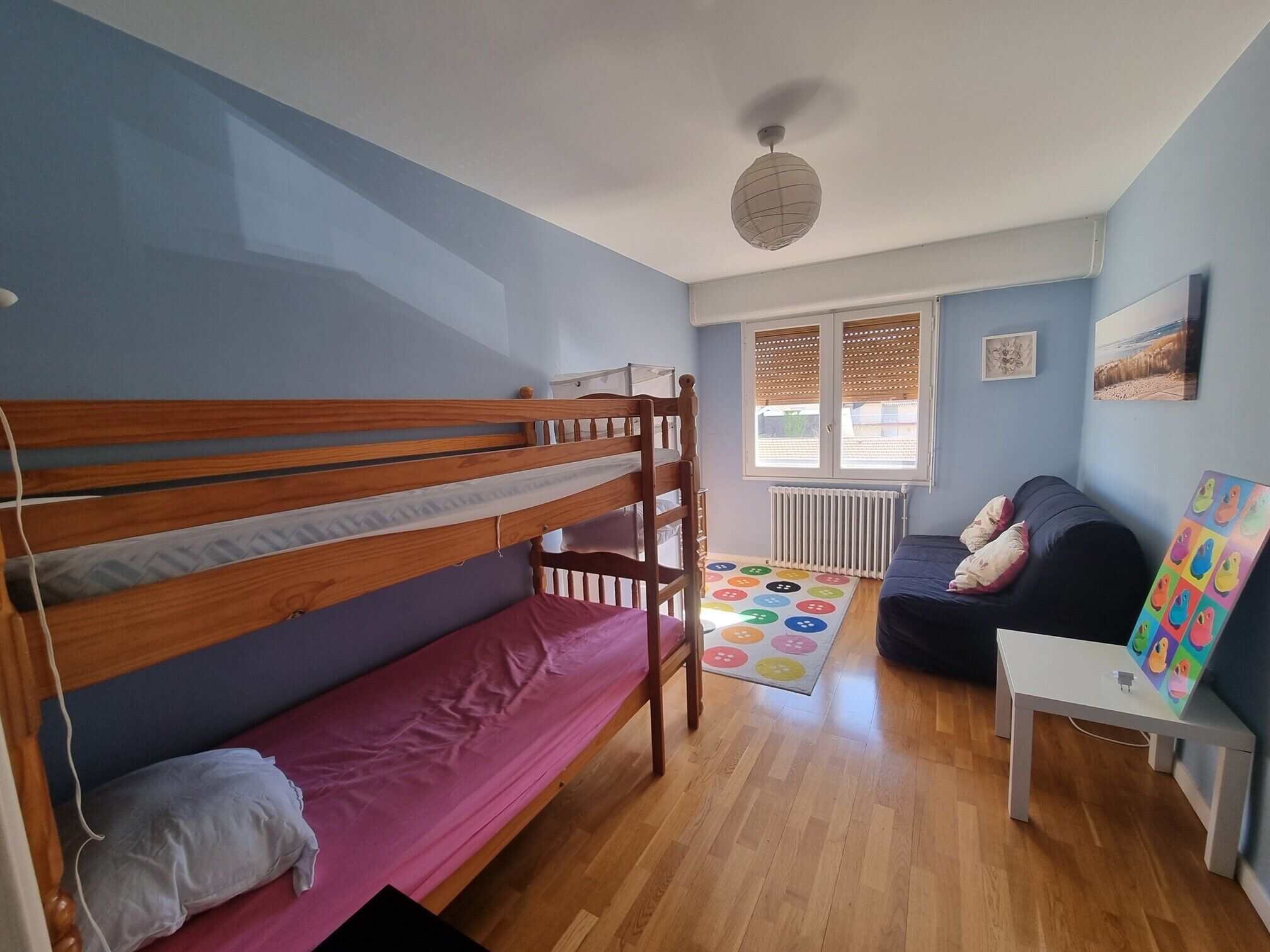 A room with a bunk bed, a small table, a couch, and a radiator.