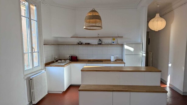 Cucina con mobili bianchi, un piano di lavoro in legno, una lampada a sospensione e un termosifone.
