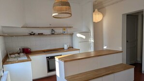 Una cucina compatta con piano di lavoro in legno, mobili bianchi, forno integrato e lampadario.