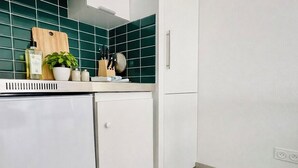 Een keuken met witte kasten, een groene spatwand, een houten snijplank, een potplant en keukengerei.