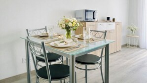 Een moderne eethoek met een glazen tafel, metalen stoelen, een bloevas en een magnetron op de achtergrond.