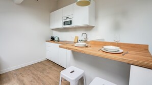 A modern kitchen with white cabinets, a wooden countertop, a sink, and a small stool. - Bright Studio at Nation, Paris 12th (Paris)