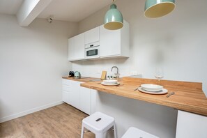 Eine moderne Küche mit weißen Schränken, einer Holz Arbeitsplatte, einer Spüle und einem kleinen Hocker.