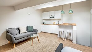 A compact living space with a sofa, a small coffee table, a kitchen area with a microwave and bar stools, and a hanging light fixture. - Bright Studio at Nation, Paris 12th (Paris)