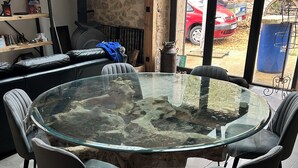 A round glass-top table with four chairs, a stone wall, a staircase, and a view of a red car outside. - Ma Lozerienne near Banassac, A75, ideal place for a get-together. (Saint-Saturnin)