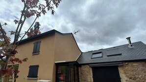 A house with a beige exterior, a stone wall, a black garage door, a small window, and a table with chairs outside. - Ma Lozerienne near Banassac, A75, ideal place for a get-together. (Saint-Saturnin)