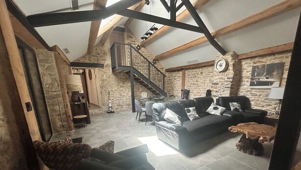 A spacious living area with a stone wall, a black leather sofa, a wooden coffee table, and a staircase with a metal railing. - Ma Lozerienne near Banassac, A75, ideal place for a get-together. (Saint-Saturnin)