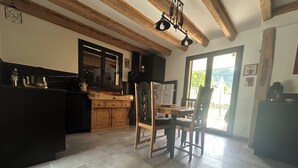 A kitchen with wooden cabinets, a dining table with chairs, and a view of the outdoors through a door. - Ma Lozerienne near Banassac, A75, ideal place for a get-together. (Saint-Saturnin)