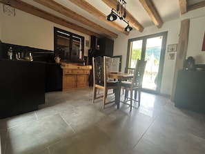 A kitchen with wooden cabinets, a dining table with chairs, and a view of the outdoors through a door. - Ma Lozerienne near Banassac, A75, ideal place for a get-together. (Saint-Saturnin)