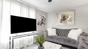 Ett vardagsrum med en grå soffa, en platt-TV, en krukväxt och abstrakt konst på väggarna.