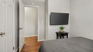 A bedroom with a bed, a television on the wall, a small table with a plant, and a door leading to another room. - Furnished 3BR Corporate Rental in Petersburg (Petersburg)