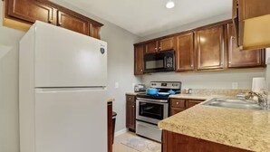 A kitchen with wooden cabinets, a white refrigerator, a microwave, a stove, and a granite countertop. - Furnished 3BR Corporate Rental in Petersburg (Petersburg)
