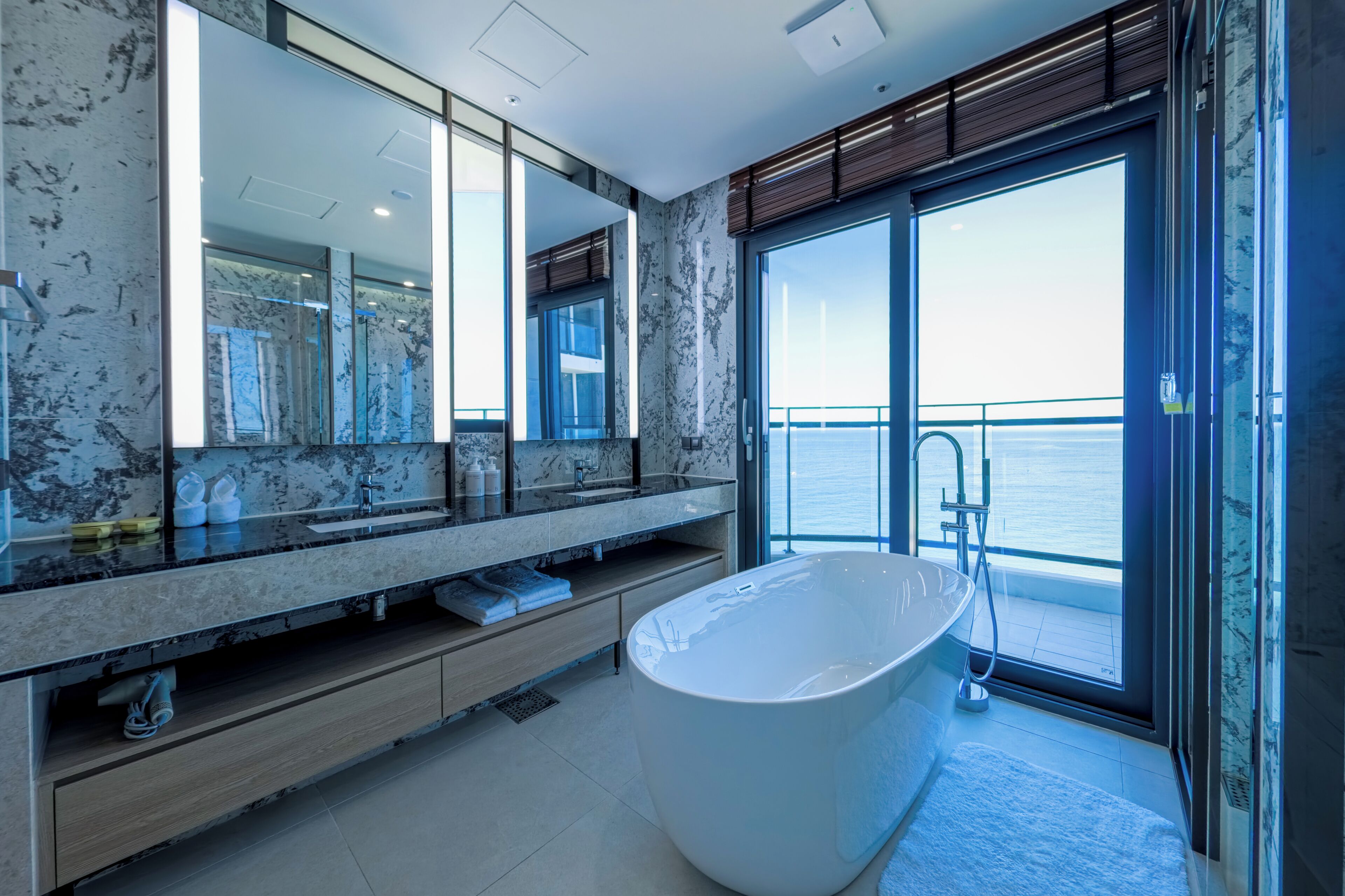 A modern bathroom with a large bathtub, a marble vanity, and a large mirror.