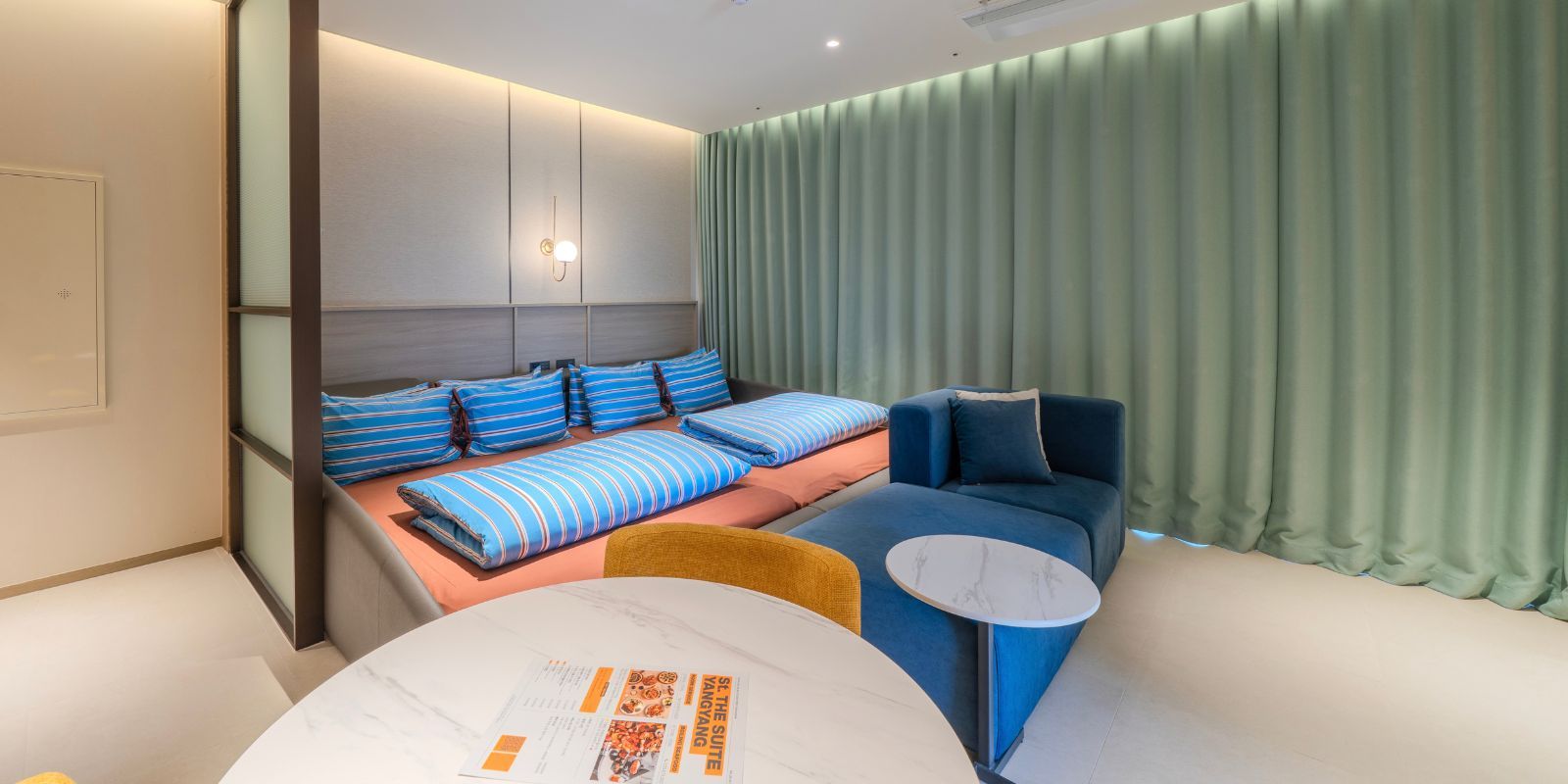 Una habitación de hotel moderna con una cama, un sofá, una mesita y una cortina.