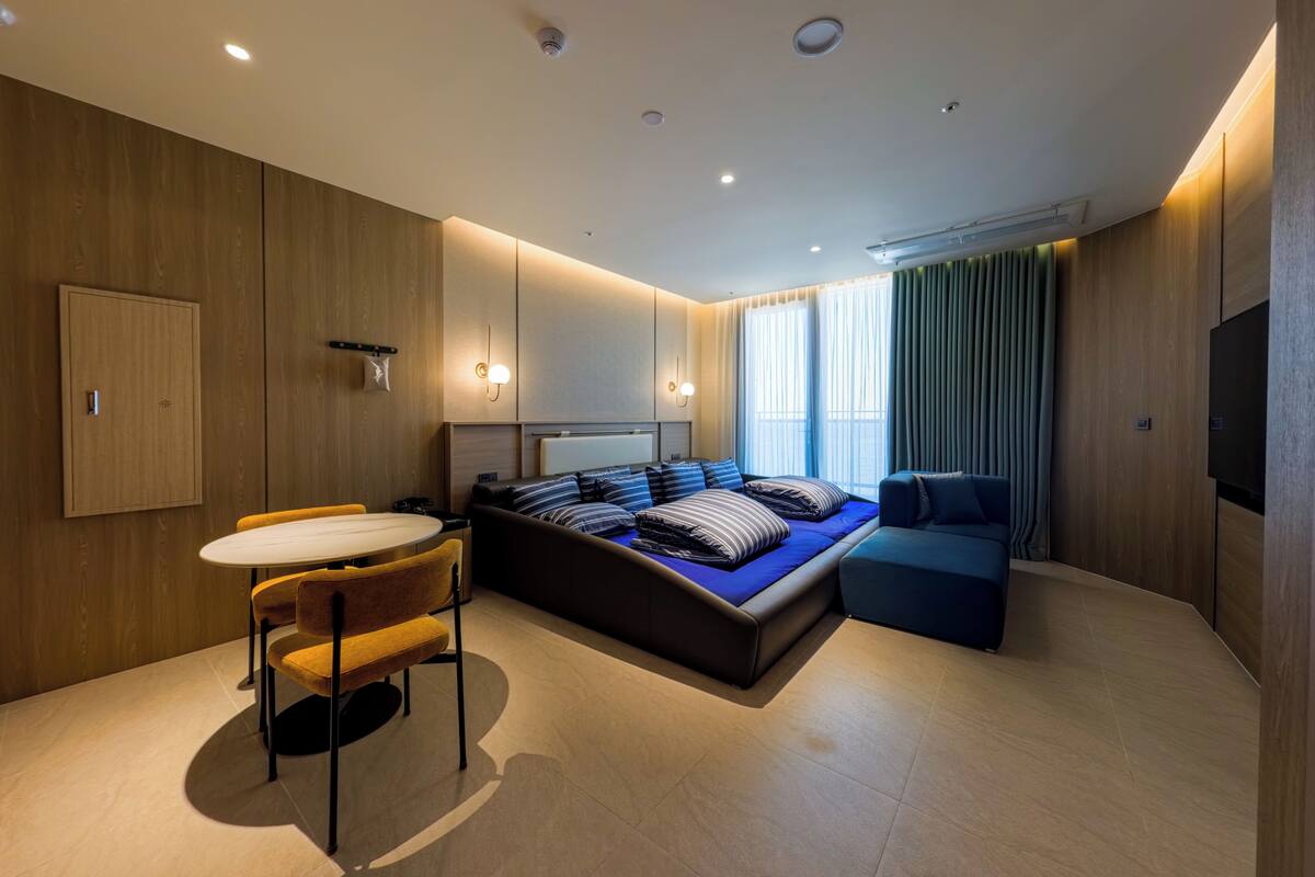 Ein modernes Hotelzimmer mit Bett, einer Couch, einem Esstisch und einem Fernseher.