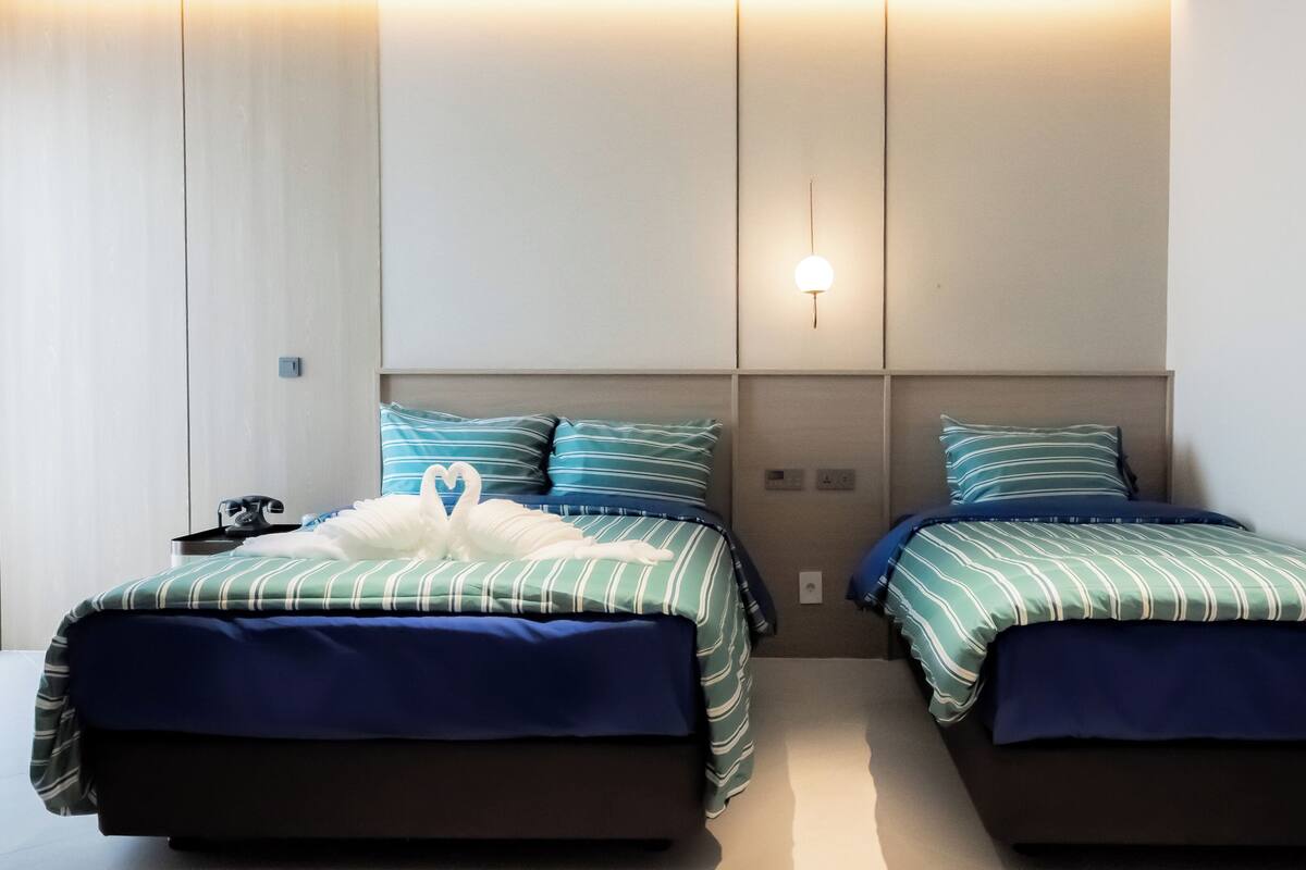 Ein Hotelzimmer mit zwei Betten, gestreifter Bettwäsche, einer herzförmigen Dekoration, einem Telefon und einer Wandleuchte.