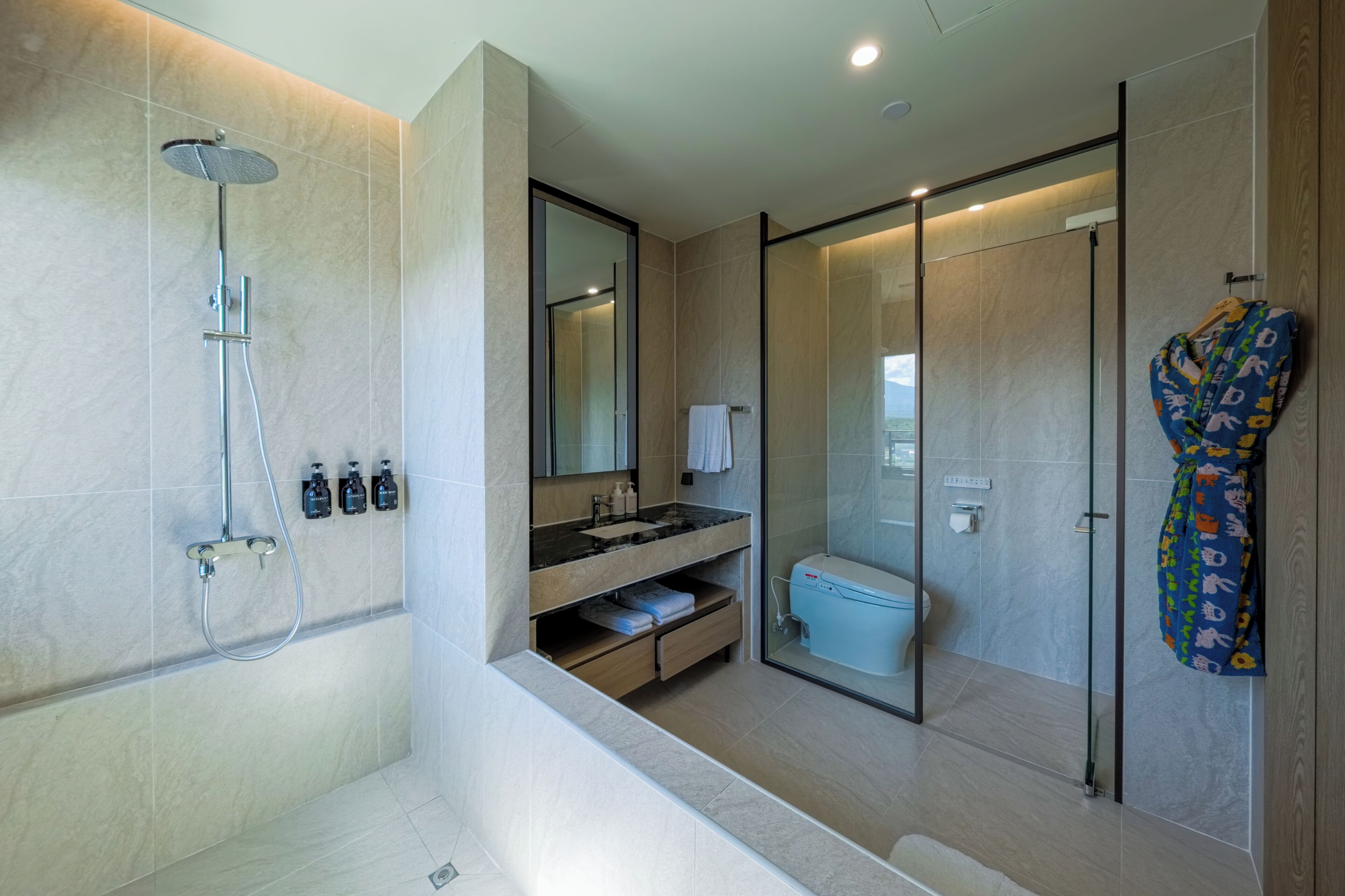 Un baño moderno con ducha de vidrio, tocador con espejo y retrete.