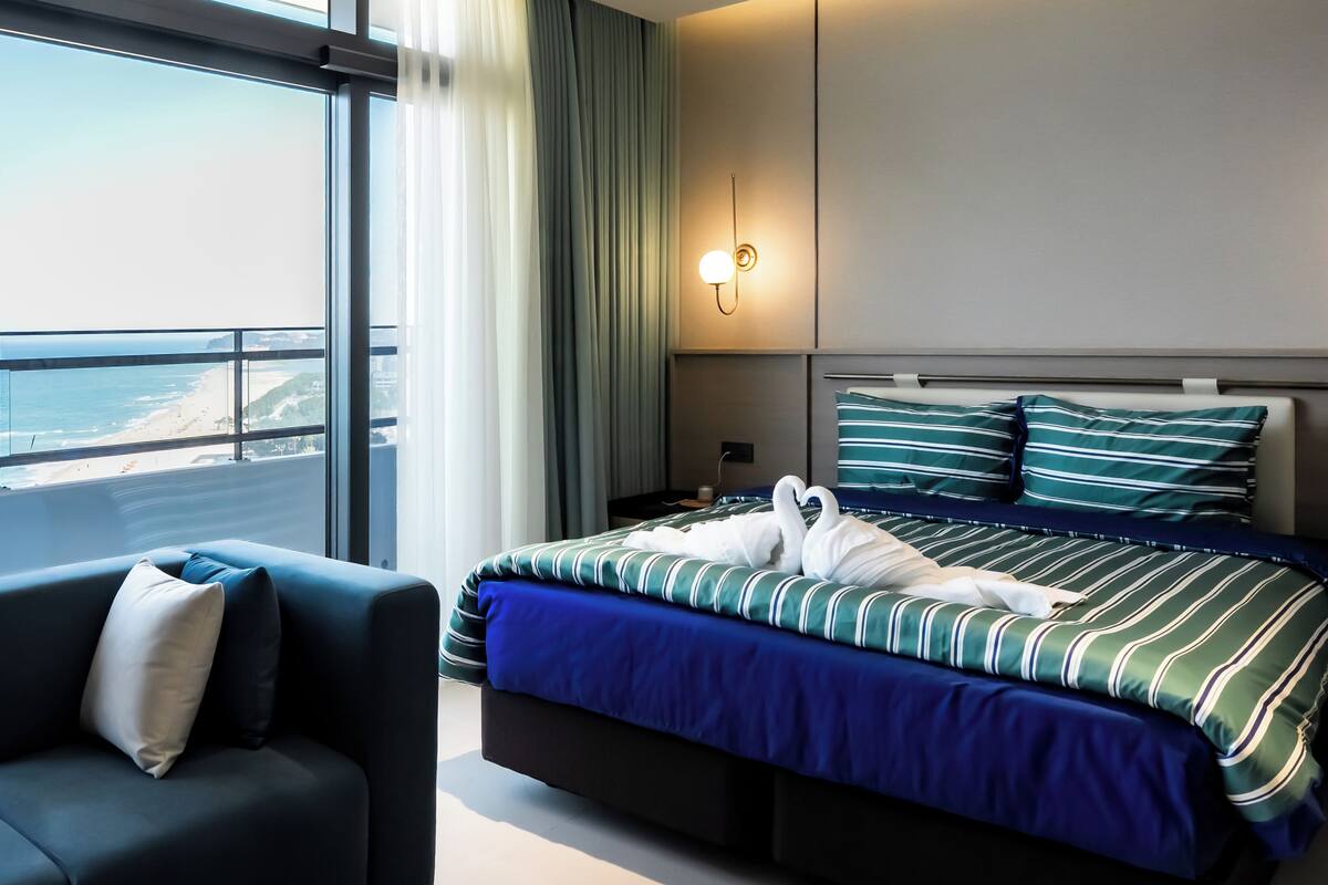 Ein Hotelzimmer mit Bett, Stuhl, Nachttisch, Lampe und Blick auf den Ozean.