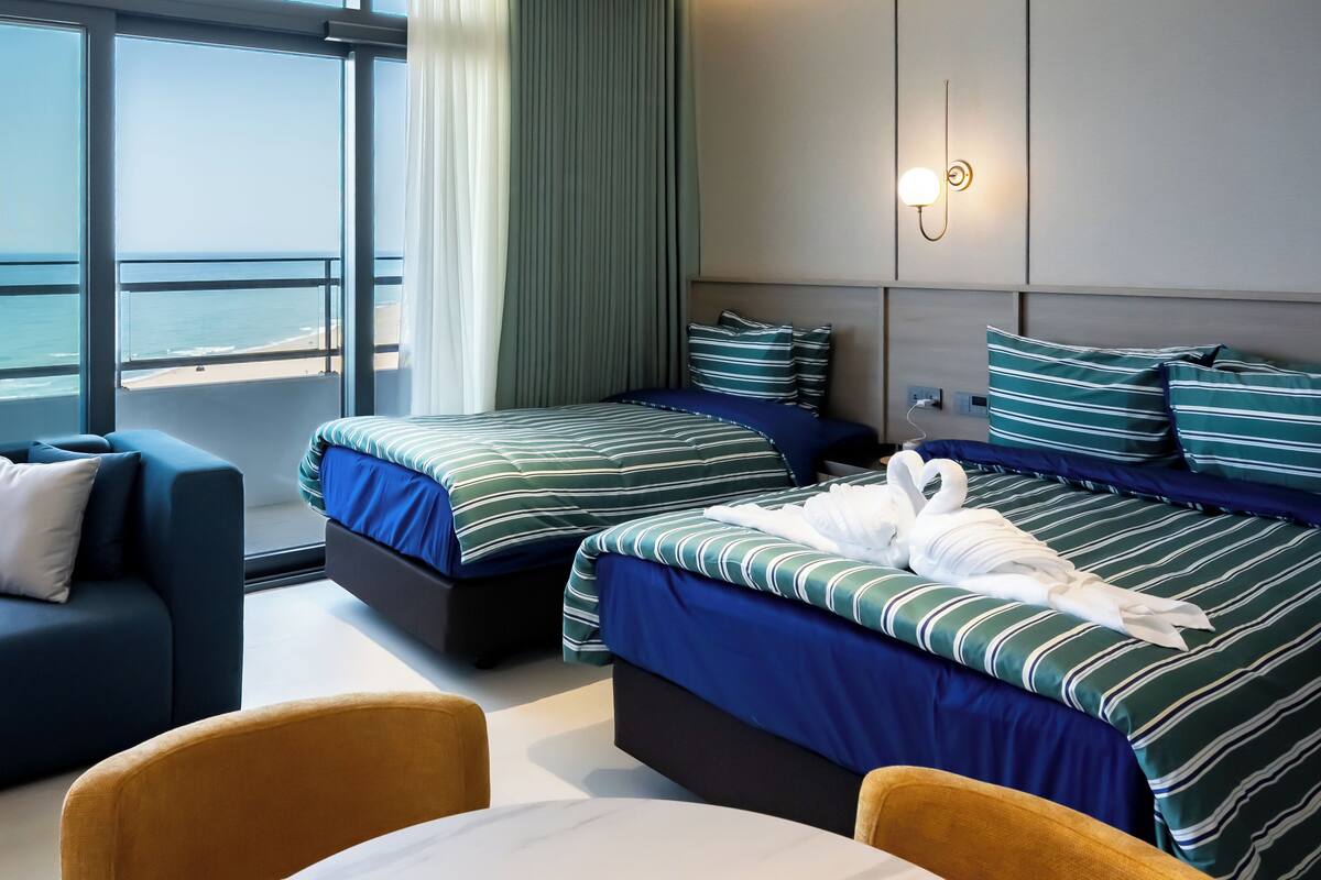 Ein Hotelzimmer mit zwei Betten, einem Sofa, einem Tisch und Blick auf den Ozean.