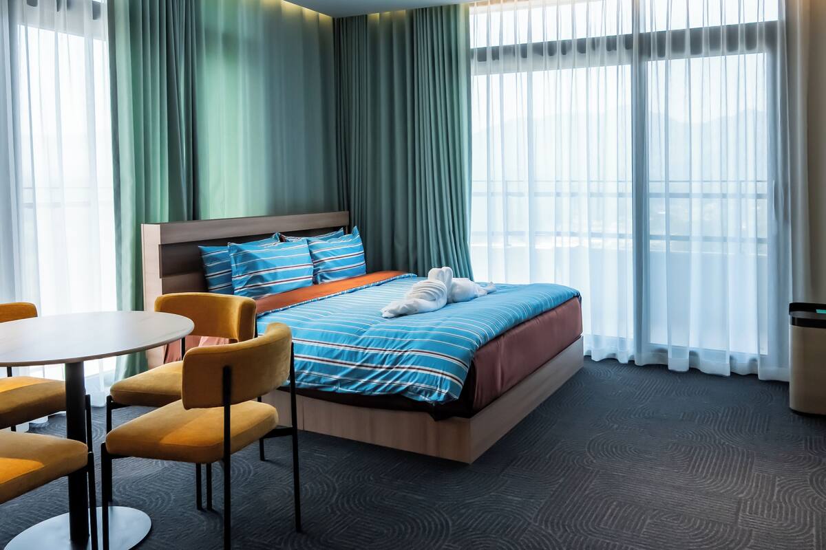 Ein Hotelzimmer mit einem Bett, einem Schreibtisch, Stühlen, einem Fernseher und großen Fenstern.