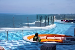 A pool area with a circular seating area and a glass barrier overlooking the ocean.