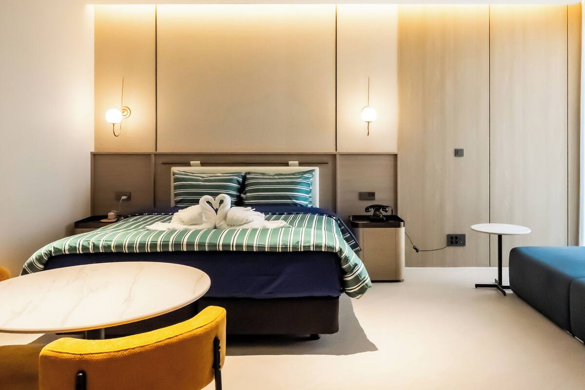 Ein Hotelzimmer mit einem Bett, einem Nachttisch, einem Sessel, einem kleinen runden Tisch, einer Couch und einer Wandlampe.