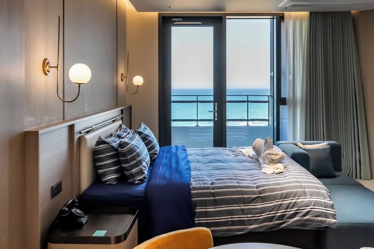 Ein Hotelzimmer mit Bett, Nachttischen, einer Sitzecke, einem kleinen Tisch und Meerblick.