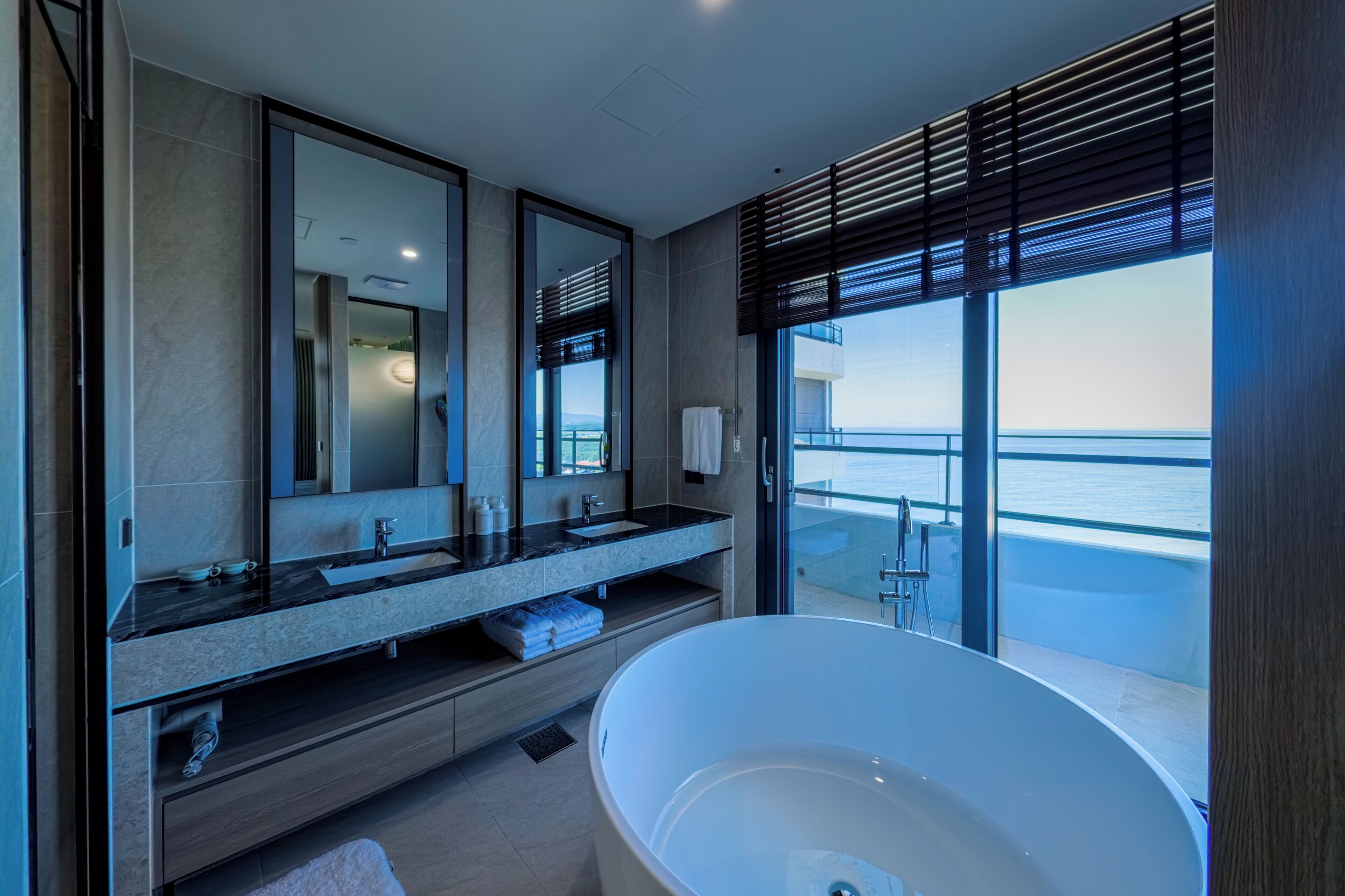 Een moderne badkamer met een groot bad, een dubbele wastafel met spiegel, en uitzicht op zee.