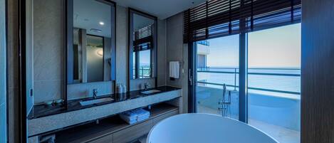 Een moderne badkamer met een groot bad, een dubbele wastafel met spiegel, en uitzicht op zee.