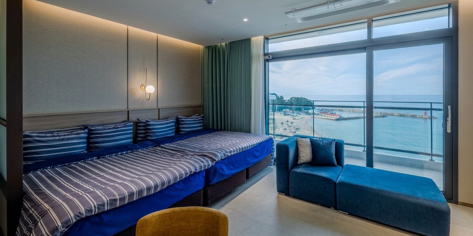 Una habitación de hotel moderna con una cama grande, un sofá y un balcón con vista al mar.