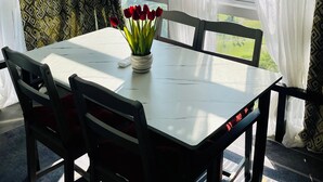 Ein Zimmer mit Tisch, Stühlen, einer Vase mit roten Blumen und Blick durch große Fenster.