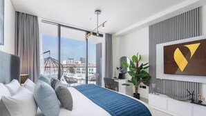 A modern hotel room with a large bed, a desk, a chair, a potted plant, and a city view. - Vogue | Binghatti Galaxy JVC near Circle Mall (Dubai)
