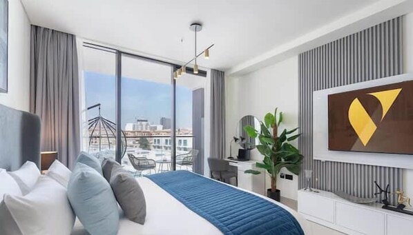 Habitación de hotel moderna con una cama grande, un escritorio, una silla, una planta en maceta y vistas a la ciudad.