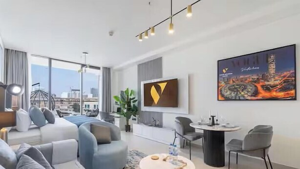 A modern hotel room with a large window, a sofa, a dining table, and a painting on the wall. - Vogue | Binghatti Galaxy JVC near Circle Mall (Dubai)
