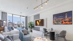 Una habitación de hotel moderna con un ventanal grande, un sofá, una mesa de comedor y un cuadro en la pared.