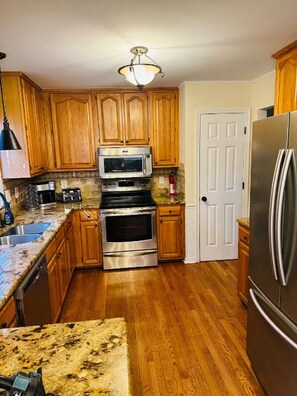 A kitchen with wooden cabinets, a stainless steel refrigerator, a microwave, an oven, and a granite countertop. - MidTerm Housing  Utilities Included Move-In Ready (Prince George)