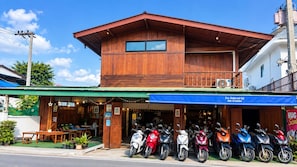 Un edificio de madera con toldo verde, un acceso cubierto y una fila de scooters estacionados.