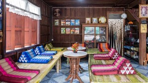 Una habitación tradicional con paredes y techo de madera, y piso de baldosas. Hay varios sofás coloridos de tejido artesanal y una mesita redonda con un florero.