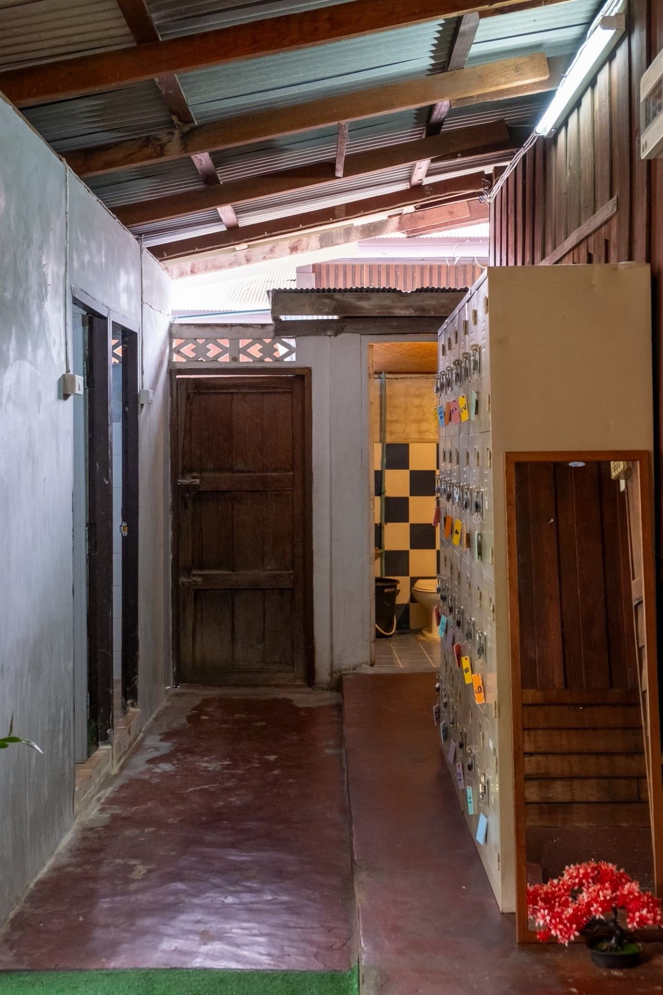 Un pasillo estrecho con un muro a cuadros, una puerta de madera y un armario metálico con llaves.
