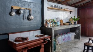 Una cocina rústica con ollas colgantes, un estante de madera con diversos objetos y un salpicadero de azulejos.