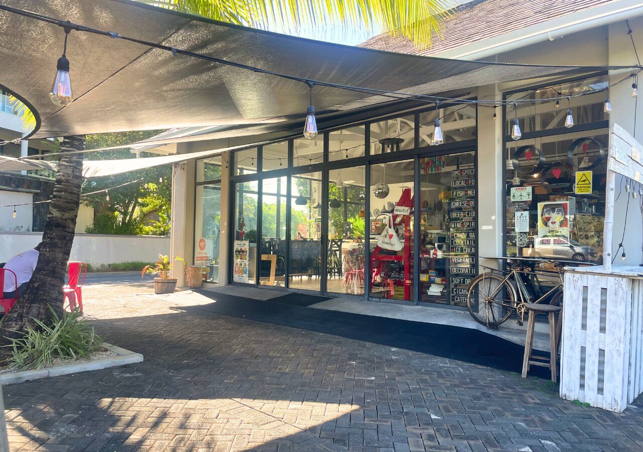 A storefront with large windows, a bicycle, and a signboard listing various items for sale.