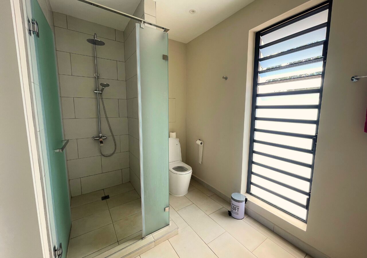 Ein Badezimmer mit Glasdusche, Toilette und Fenster mit Jalousien.