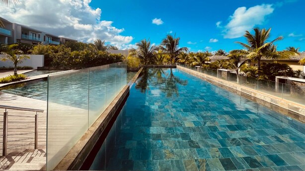 A swimming pool with clear water, surrounded by palm trees and a modern building. - Azuri Resort Villa: Pool, Golf & Beach Club (Rivière du Rempart)