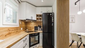 Eine moderne Küche mit weißen Schränken, einem schwarzen Kühlschrank, einer Holzarbeitsplatte und einem Essbereich mit Tisch und Stühlen.