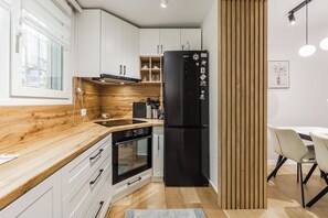 A modern kitchen with white cabinets, a black refrigerator, a wooden countertop, and a dining area with a table and chairs. - Siara Apartment by Kondo Stays (Tiranë)
