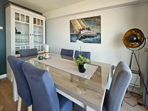 Un espace repas comprenant une table, des chaises, un buffet, un tableau et un lampadaire.