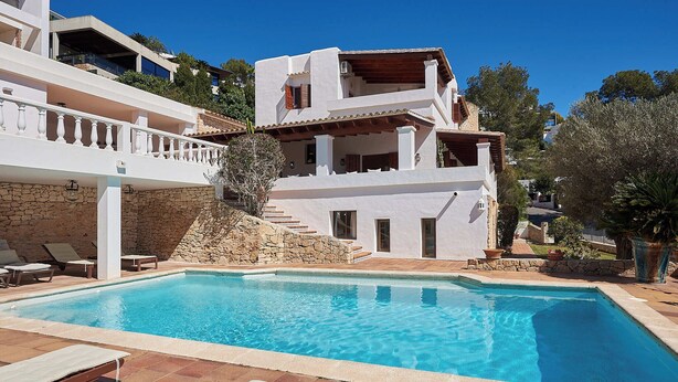 Ein Pool mit Liegestühlen, einer Steinmauer und einem mehrstöckigen Gebäude mit Balkonen.