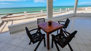 Überdachter Außenbereich mit Tisch und Stühlen mit Blick auf einen Strand.