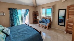 Ein Schlafzimmer mit einem Bett, einem Sessel, einem Ventilator und Blick auf den Ozean.